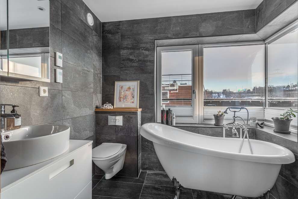 Inredning av ett modernt mellanstort vit vitt badrum, med släta luckor, vita skåp, ett badkar med tassar, en dusch/badkar-kombination, en vägghängd toalettstol, grå kakel, skifferkakel, grå väggar, skiffergolv, ett fristående handfat, bänkskiva i kvarts, grått golv och med dusch som är öppen