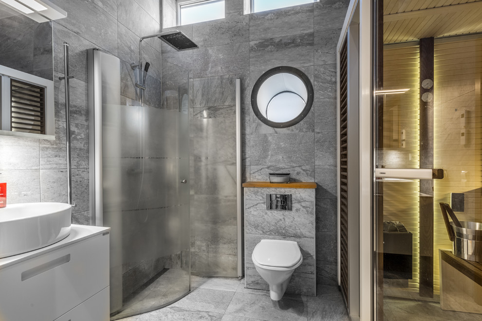 Photo of a large contemporary sauna bathroom in Stockholm with flat-panel cabinets, white cabinets, a wall mounted toilet, grey walls, a vessel sink, a hinged door, a built-in shower, grey tiles, grey floors and white worktops.