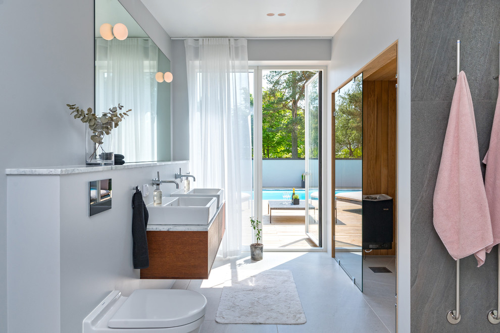 Réalisation d'une grande salle de bain principale design en bois foncé avec un placard à porte plane, un mur gris, une vasque et un sol gris.