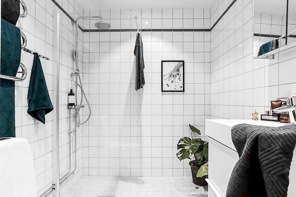 Foto på ett nordiskt vit badrum med dusch, med vita skåp, en dusch i en alkov, en toalettstol med hel cisternkåpa, vit kakel, cementkakel, vita väggar, cementgolv, ett nedsänkt handfat, vitt golv, med dusch som är öppen, släta luckor och kaklad bänkskiva