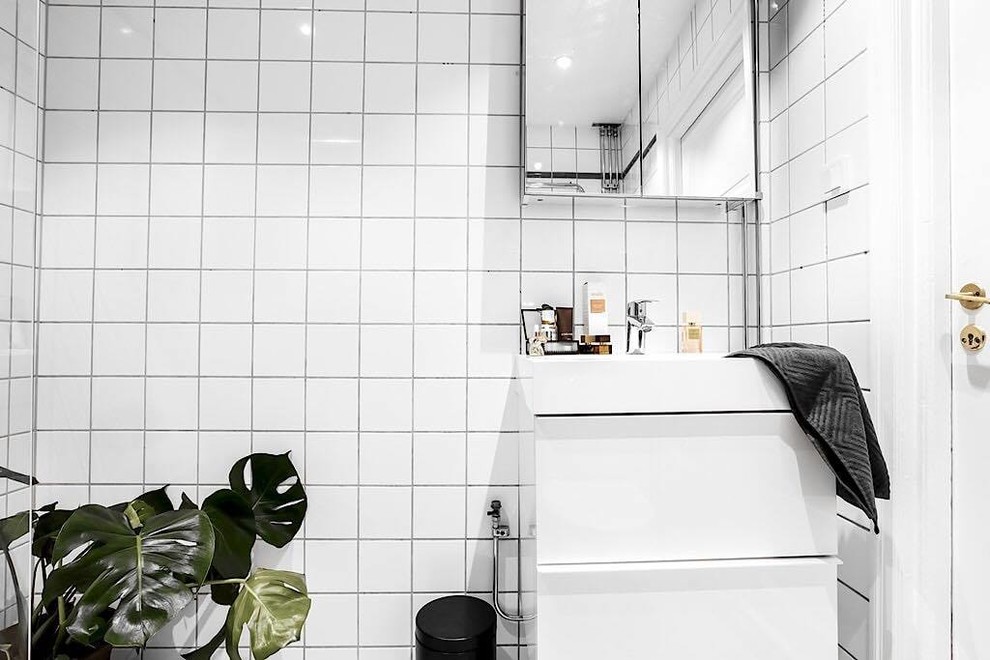 Nordisk inredning av ett vit vitt badrum, med vita skåp, vit kakel, keramikplattor, vita väggar, ett avlångt handfat och kaklad bänkskiva