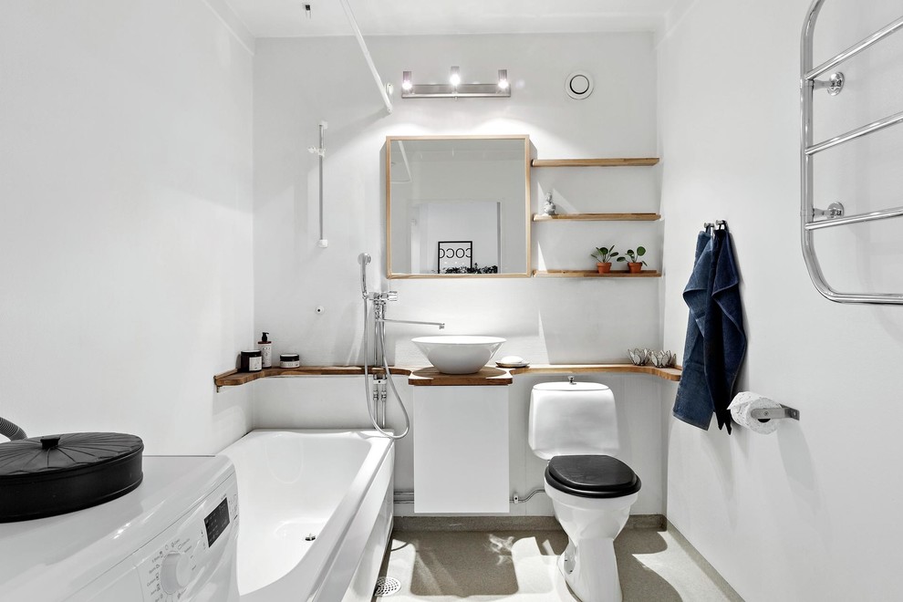 Skandinavisk inredning av ett mellanstort brun brunt badrum, med en dusch/badkar-kombination, vita väggar, linoleumgolv, ett fristående handfat, träbänkskiva, grått golv, släta luckor, vita skåp, ett hörnbadkar, en toalettstol med separat cisternkåpa och dusch med duschdraperi