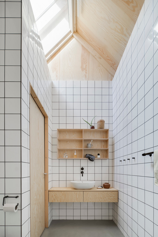 Mid-sized danish ceramic tile concrete floor bathroom photo in Malmo with flat-panel cabinets, light wood cabinets, white walls, a vessel sink and wood countertops