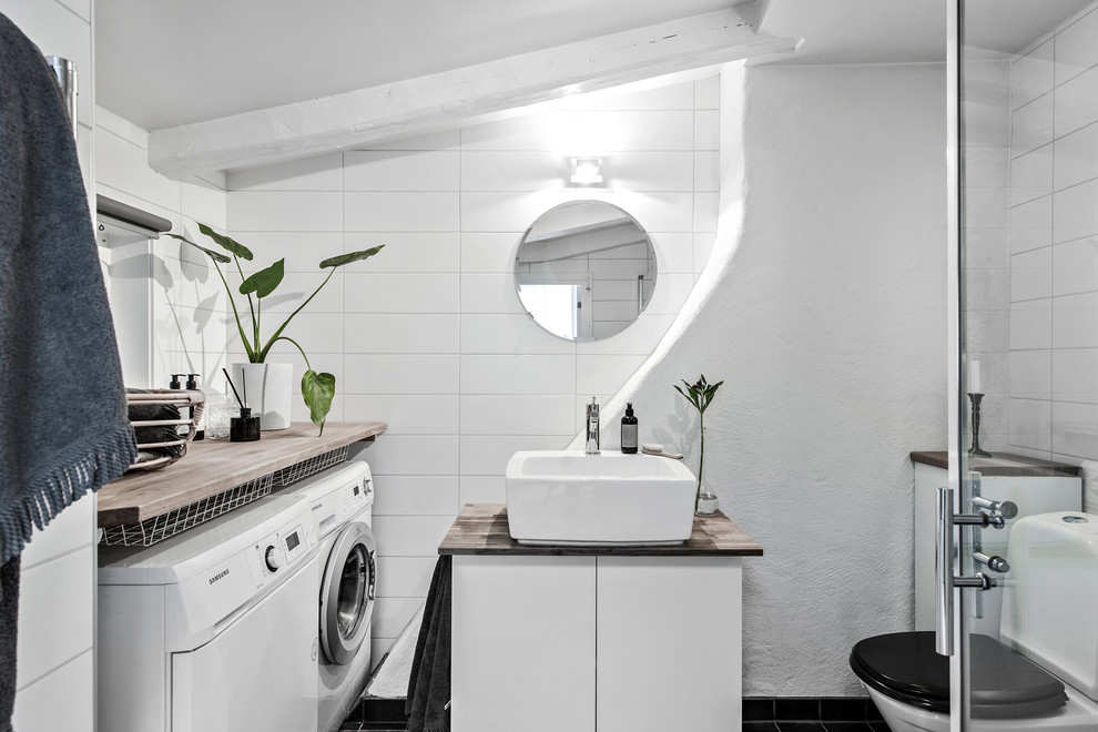 Idéer för att renovera ett minimalistiskt beige beige badrum med dusch, med släta luckor, vita skåp, en toalettstol med separat cisternkåpa, vit kakel, vita väggar, ett fristående handfat, träbänkskiva och svart golv