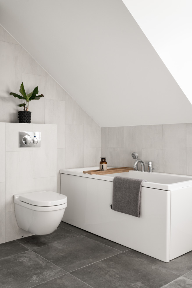 Kleines Skandinavisches Badezimmer mit Wandtoilette, grauen Fliesen, weißen Fliesen, grauem Boden, Einbaubadewanne und weißer Wandfarbe in Stockholm