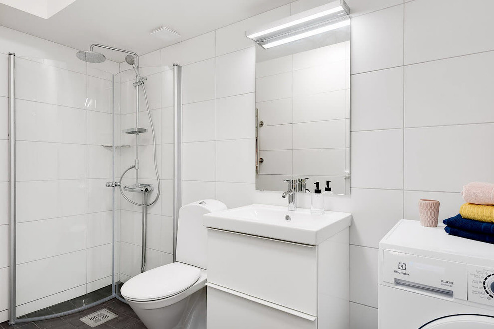 Example of a small trendy 3/4 white tile and ceramic tile black floor corner shower design in Stockholm with flat-panel cabinets, white cabinets, a one-piece toilet, white walls, a trough sink, tile countertops and a hinged shower door