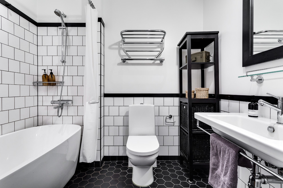 ストックホルムにある高級な中くらいな北欧スタイルのおしゃれなバスルーム (浴槽なし) (シャワー付き浴槽	、黒いタイル、白い壁、磁器タイルの床、横長型シンク、オープンシェルフ、黒いキャビネット、置き型浴槽、一体型トイレ	、シャワーカーテン) の写真