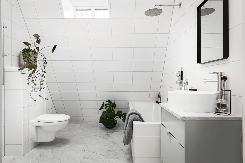 Exemple d'une salle de bain grise et blanche scandinave de taille moyenne avec un placard à porte plane, des portes de placard grises, une baignoire posée, WC suspendus, des carreaux de porcelaine, un mur blanc et un sol en marbre.