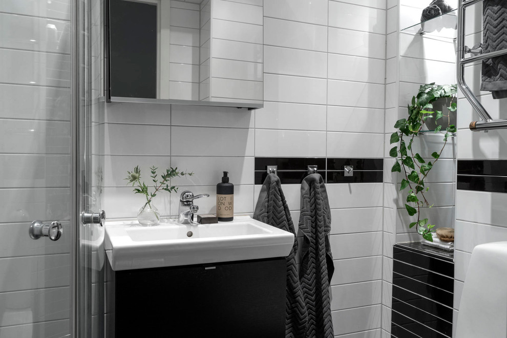 Skandinavisk inredning av ett badrum med dusch, med släta luckor, svarta skåp, en hörndusch, svart och vit kakel, ett konsol handfat och dusch med skjutdörr