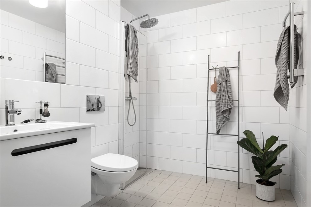 Idée de décoration pour une salle de bain nordique de taille moyenne avec un placard à porte plane, des portes de placard blanches, une douche ouverte, WC suspendus, un carrelage blanc, des carreaux de porcelaine, un mur blanc, un lavabo posé et un sol beige.