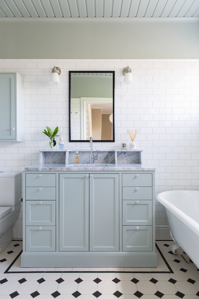 Inredning av ett klassiskt mellanstort badrum, med skåp i shakerstil, blå skåp, ett fristående badkar, grå väggar, ett undermonterad handfat, porslinskakel, klinkergolv i porslin och marmorbänkskiva