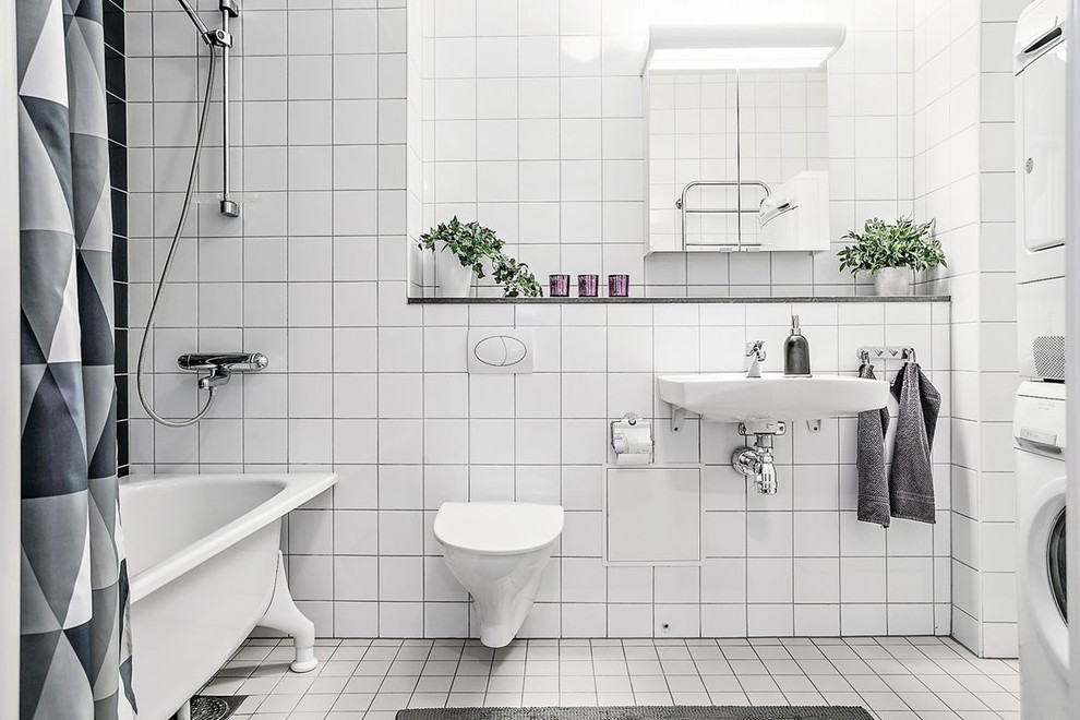 This is an example of a medium sized scandinavian ensuite bathroom in Stockholm with a freestanding bath, a wall mounted toilet, white tiles, white walls, ceramic flooring, a shower/bath combination, a wall-mounted sink, white floors, an open shower and feature lighting.