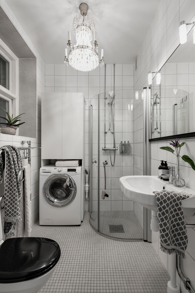 Foto på ett skandinaviskt badrum med dusch, med en hörndusch, en toalettstol med separat cisternkåpa, vit kakel, vita väggar, mosaikgolv, ett piedestal handfat, vitt golv och dusch med skjutdörr