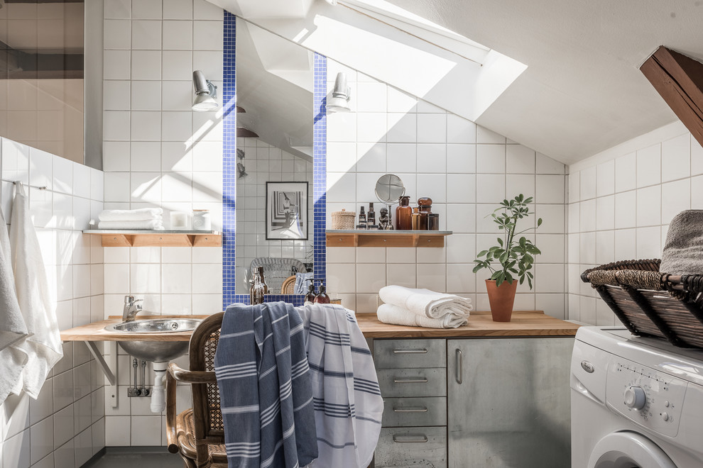 Aménagement d'une grande salle de bain industrielle avec un placard à porte plane, des portes de placard grises, un mur blanc, un lavabo posé, un plan de toilette en bois et des carreaux de céramique.