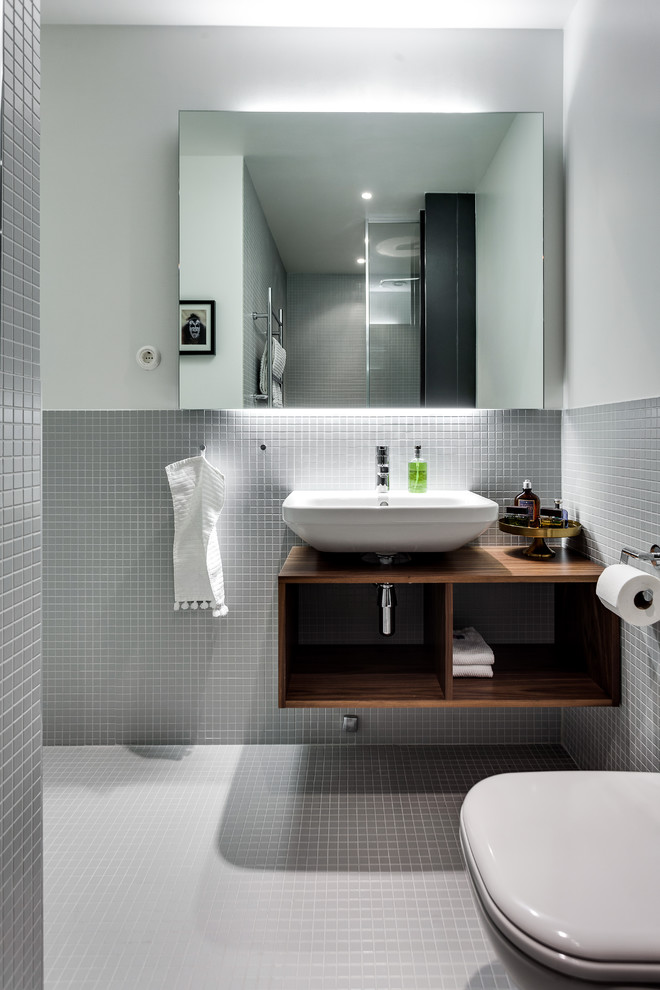 Foto på ett mellanstort nordiskt badrum med dusch, med öppna hyllor, skåp i mörkt trä, grå väggar, mosaikgolv, ett väggmonterat handfat, en toalettstol med hel cisternkåpa och träbänkskiva