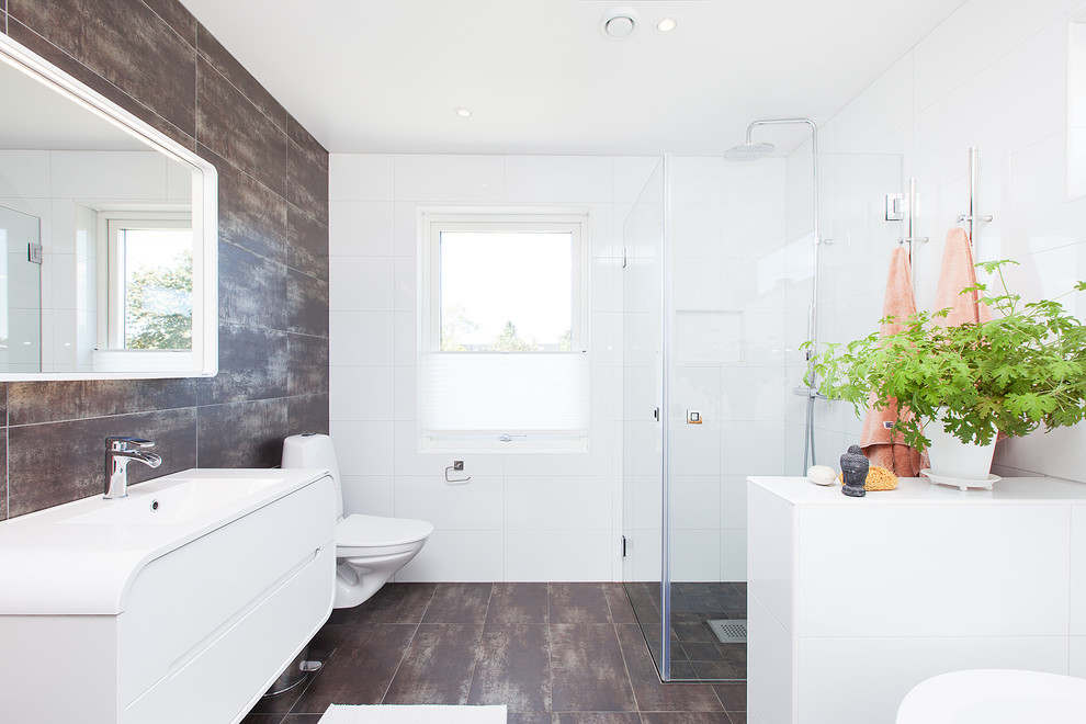 Пример оригинального дизайна: большая ванная комната в скандинавском стиле с плоскими фасадами, белыми фасадами, угловым душем, коричневой плиткой, белой плиткой, белыми стенами, подвесной раковиной, инсталляцией, полом из известняка, столешницей из известняка и душем с распашными дверями