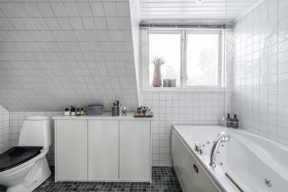 Bild på ett minimalistiskt vit vitt badrum, med vita skåp, ett hörnbadkar, en dusch/badkar-kombination, en toalettstol med hel cisternkåpa, vit kakel, vita väggar, grönt golv och med dusch som är öppen