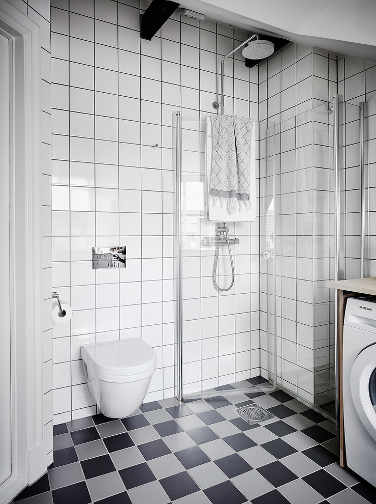 Nordisches Duschbad mit bodengleicher Dusche, Wandtoilette, weißen Fliesen, grauem Boden und Falttür-Duschabtrennung in Göteborg