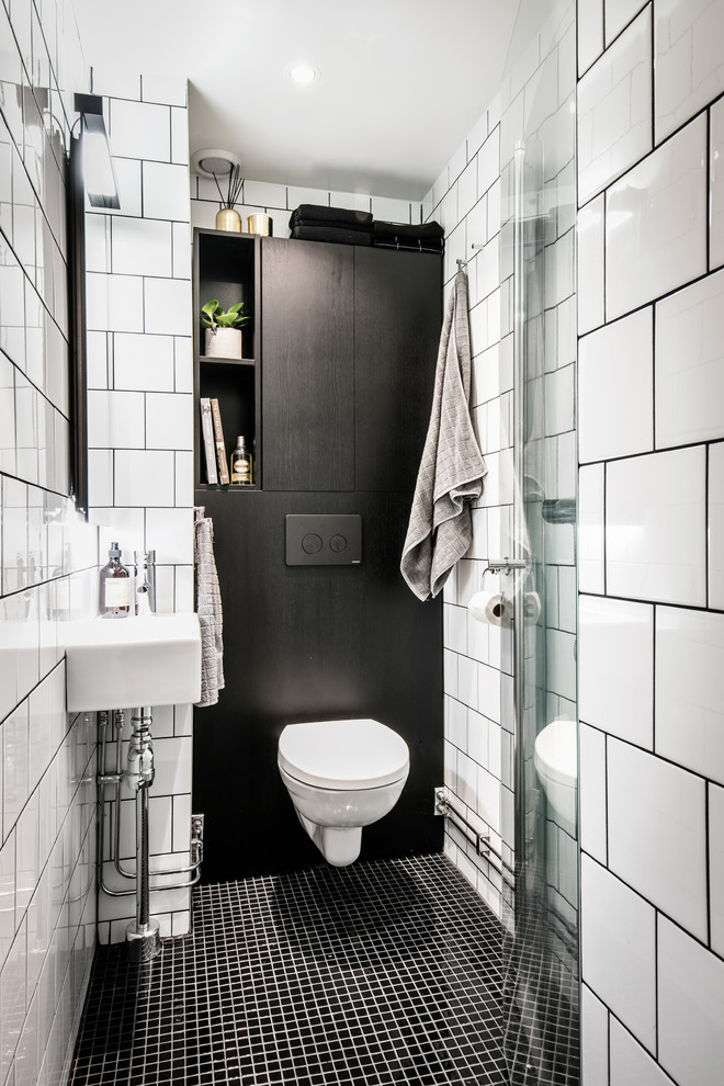 Inredning av ett minimalistiskt litet badrum med dusch, med möbel-liknande, svarta skåp, en hörndusch, en toalettstol med hel cisternkåpa, vit kakel, keramikplattor, vita väggar, mosaikgolv, ett väggmonterat handfat, svart golv och dusch med skjutdörr