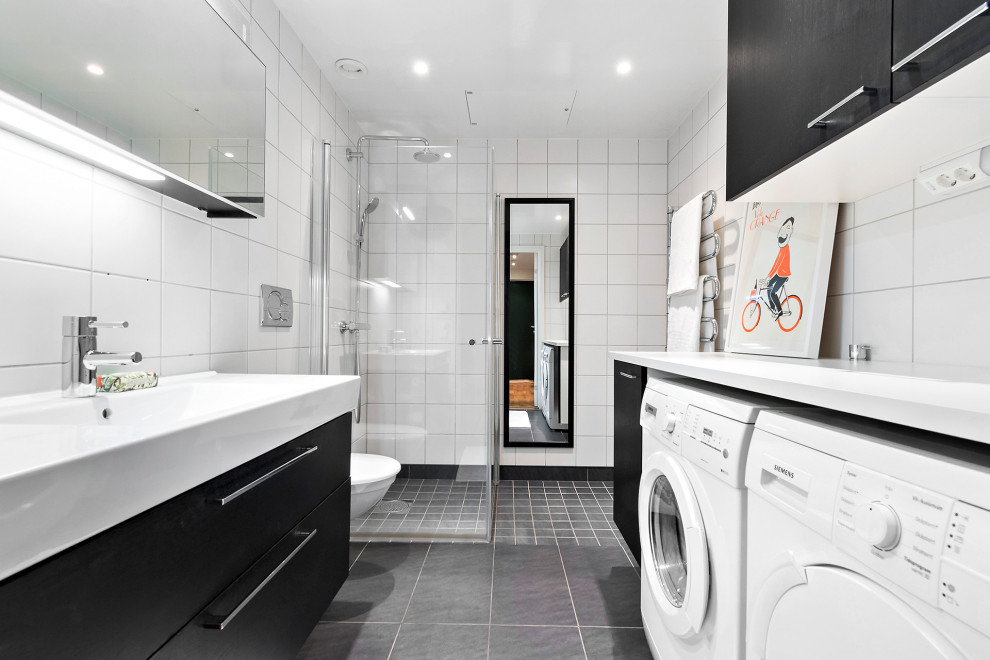 Inredning av ett modernt vit vitt badrum med dusch, med svarta skåp, en hörndusch, en vägghängd toalettstol, vit kakel, vita väggar, klinkergolv i keramik, grått golv och dusch med gångjärnsdörr