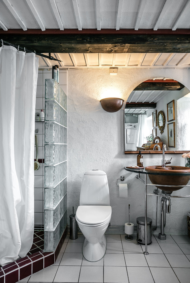 Lantlig inredning av ett litet badrum med dusch, med en hörndusch, vita väggar, ett piedestal handfat, en toalettstol med hel cisternkåpa, vit kakel, vitt golv och dusch med duschdraperi