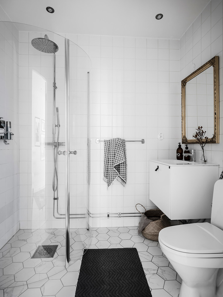 На фото: ванная комната в скандинавском стиле с плоскими фасадами, белыми фасадами, угловым душем, раздельным унитазом, белой плиткой, белыми стенами, душевой кабиной, серым полом и душем с распашными дверями