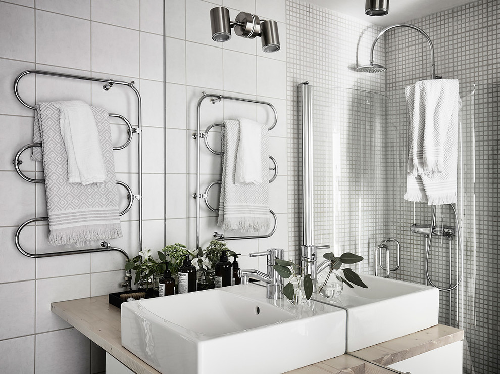 Bild på ett skandinaviskt badrum, med vit kakel, vita väggar, ett fristående handfat och träbänkskiva