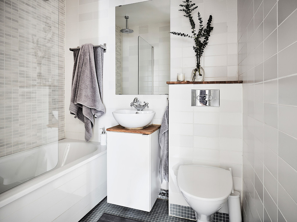 Bild på ett mellanstort minimalistiskt badrum, med släta luckor, vita skåp, ett badkar i en alkov, en dusch i en alkov, en vägghängd toalettstol, grå väggar, ett fristående handfat, träbänkskiva och med dusch som är öppen