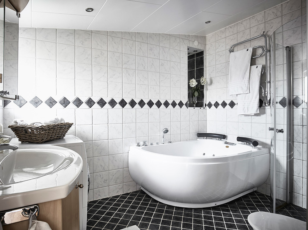 Diseño de cuarto de baño escandinavo con bañera esquinera, ducha esquinera, baldosas y/o azulejos blancos, paredes blancas, lavabo integrado y suelo negro