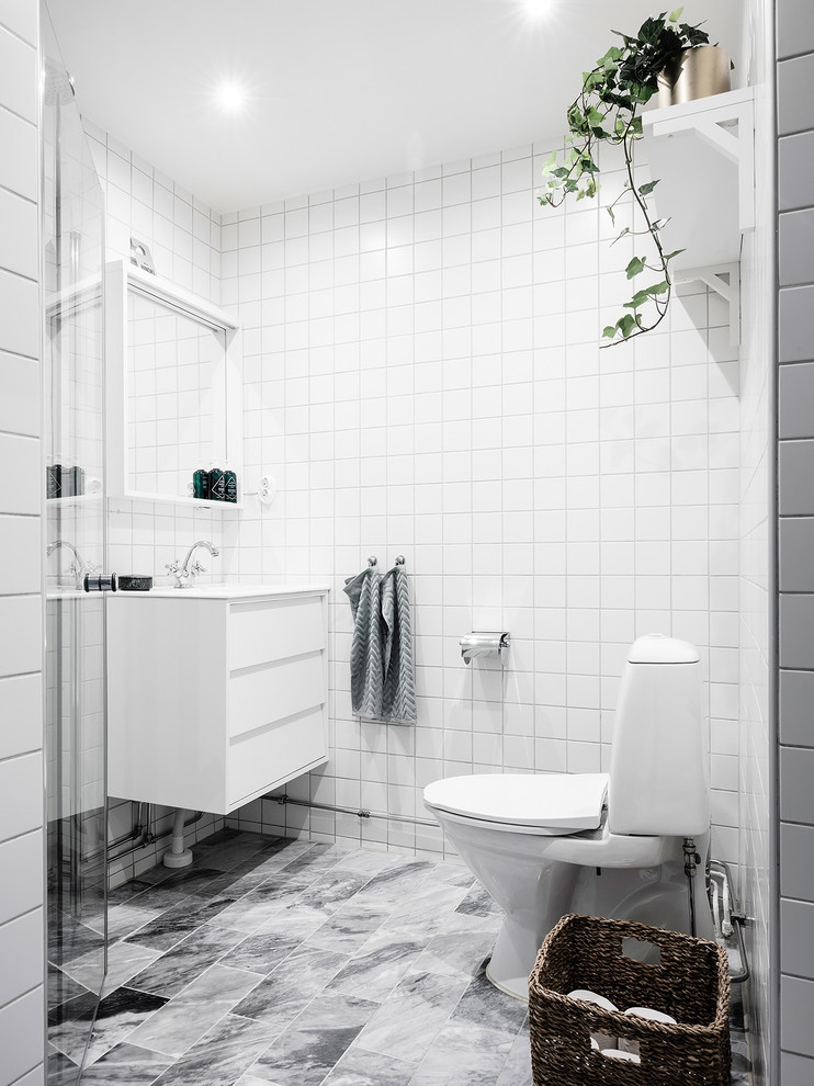 Mittelgroßes Skandinavisches Badezimmer mit flächenbündigen Schrankfronten, weißen Schränken, weißen Fliesen, weißer Wandfarbe, Wandtoilette mit Spülkasten, grauem Boden und weißer Waschtischplatte in Göteborg