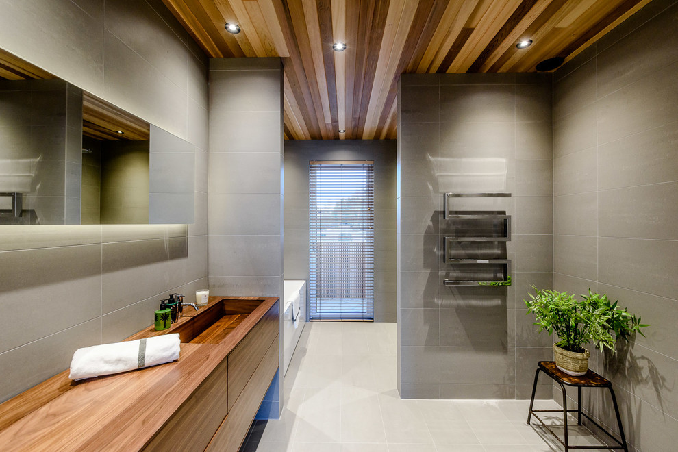 Aménagement d'une salle de bain moderne en bois brun de taille moyenne avec un placard à porte plane, un carrelage gris, un mur gris, un lavabo intégré, un plan de toilette en bois et un plan de toilette marron.