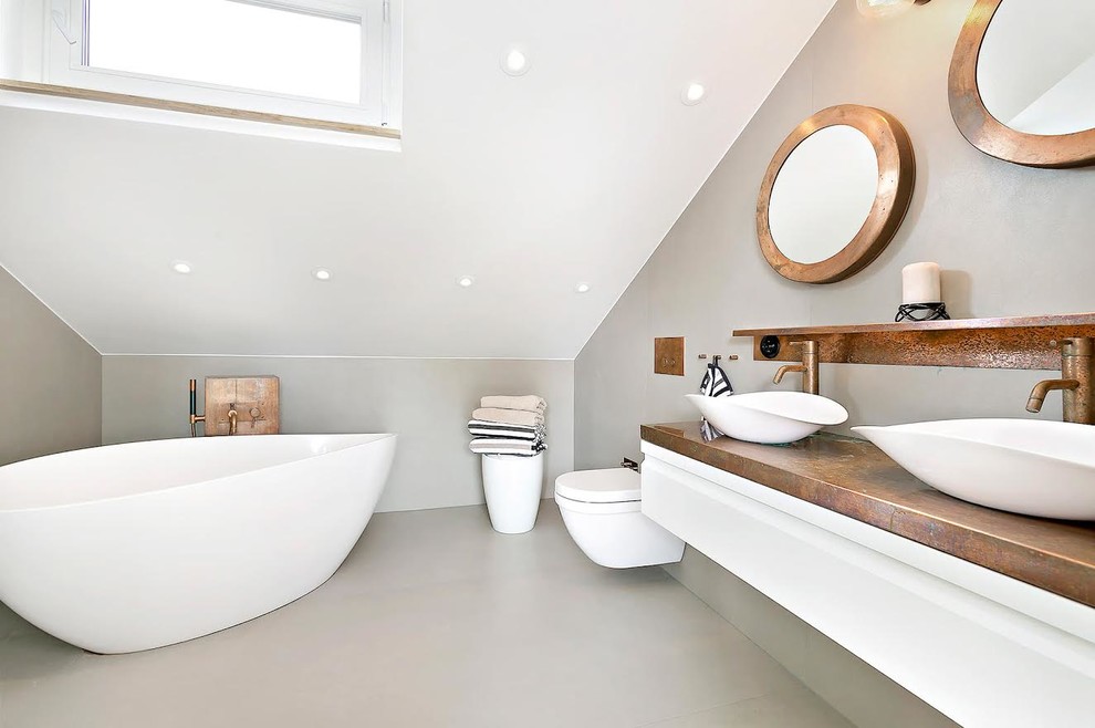 Bild på ett stort funkis badrum, med ett fristående badkar, en vägghängd toalettstol, vita väggar, betonggolv och ett fristående handfat