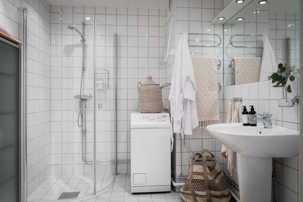 Esempio di una stanza da bagno nordica con doccia ad angolo, piastrelle bianche, lavabo a colonna, pavimento bianco, porta doccia a battente e lavanderia