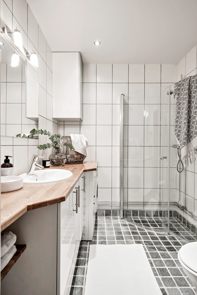 Immagine di una stanza da bagno nordica con piastrelle bianche, lavabo integrato e top in legno