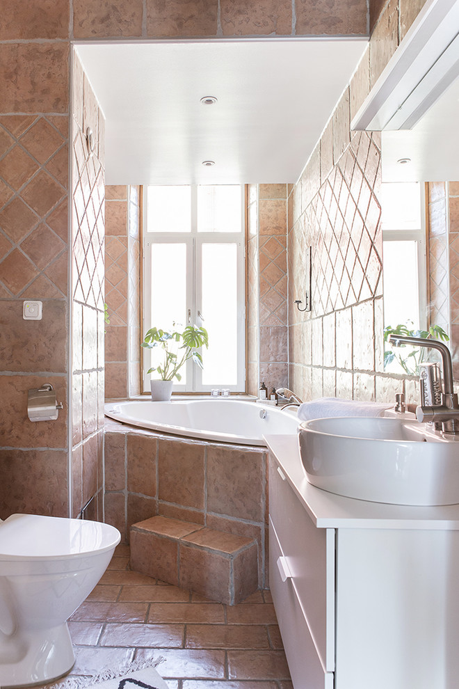 Modelo de cuarto de baño mediterráneo de tamaño medio con armarios con paneles lisos, puertas de armario blancas, bañera esquinera, sanitario de una pieza, paredes marrones y lavabo sobreencimera