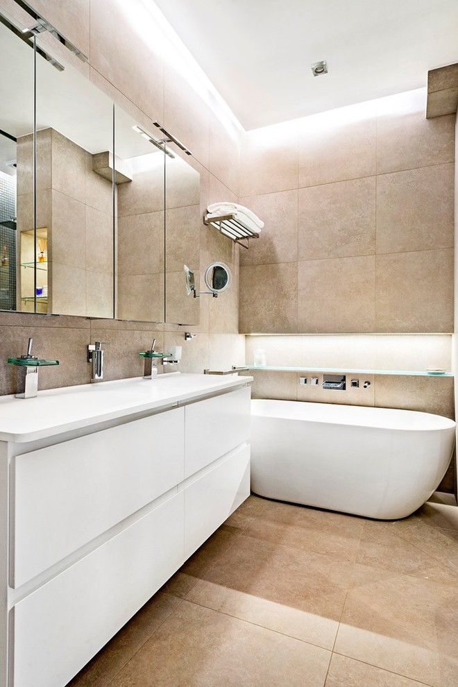 На фото: ванная комната среднего размера в стиле модернизм с плоскими фасадами, белыми фасадами, отдельно стоящей ванной, бежевыми стенами, полом из керамической плитки и монолитной раковиной