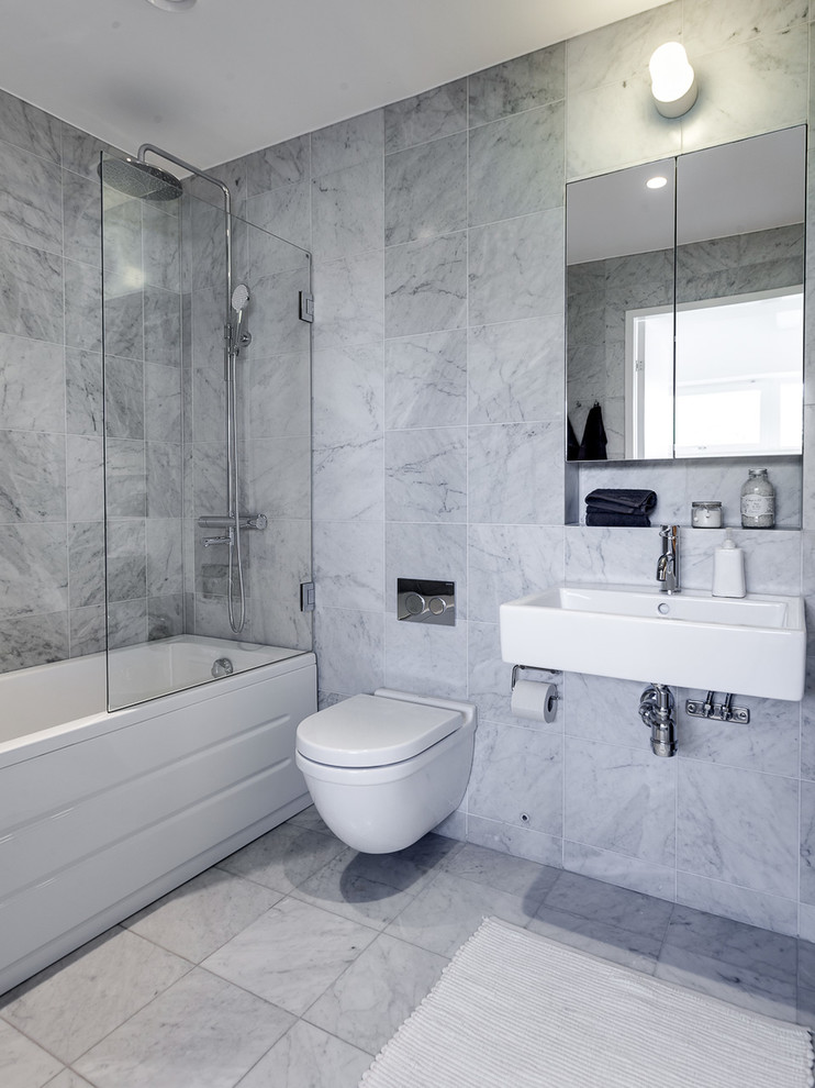Diseño de cuarto de baño escandinavo grande con armarios con paneles lisos, bañera encastrada sin remate, combinación de ducha y bañera, sanitario de pared, baldosas y/o azulejos grises, paredes grises, suelo de baldosas de cerámica, lavabo integrado y ducha abierta