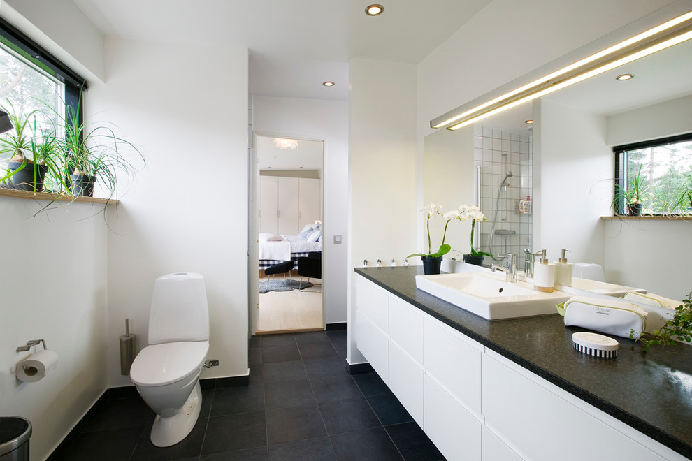 Idéer för ett stort modernt badrum, med släta luckor, vita skåp, en toalettstol med separat cisternkåpa, svart kakel, vita väggar, ett nedsänkt handfat, kalkstensgolv och granitbänkskiva