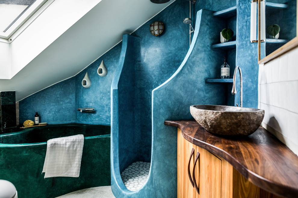 Cette image montre une salle de bain nordique en bois brun de taille moyenne avec un placard à porte plane, une baignoire posée, une douche ouverte, un mur bleu, une vasque et un plan de toilette en bois.
