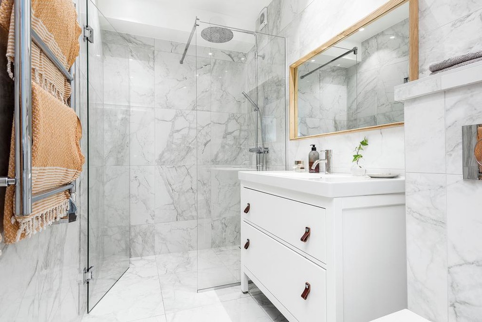 Foto på ett mellanstort nordiskt badrum med dusch, med släta luckor, vita skåp, vit kakel, marmorkakel, vita väggar, marmorgolv, vitt golv, dusch med gångjärnsdörr och en kantlös dusch