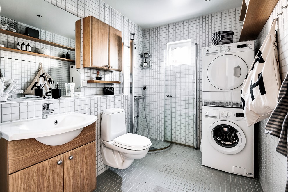 Modelo de cuarto de baño escandinavo con armarios con paneles lisos, puertas de armario de madera oscura, ducha esquinera, baldosas y/o azulejos blancos, baldosas y/o azulejos en mosaico, lavabo encastrado, suelo gris y tendedero