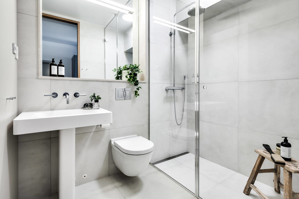 Exempel på ett mellanstort skandinaviskt badrum med dusch, med en hörndusch, vit kakel, vita väggar, en vägghängd toalettstol, cementkakel, ett piedestal handfat, grått golv och med dusch som är öppen