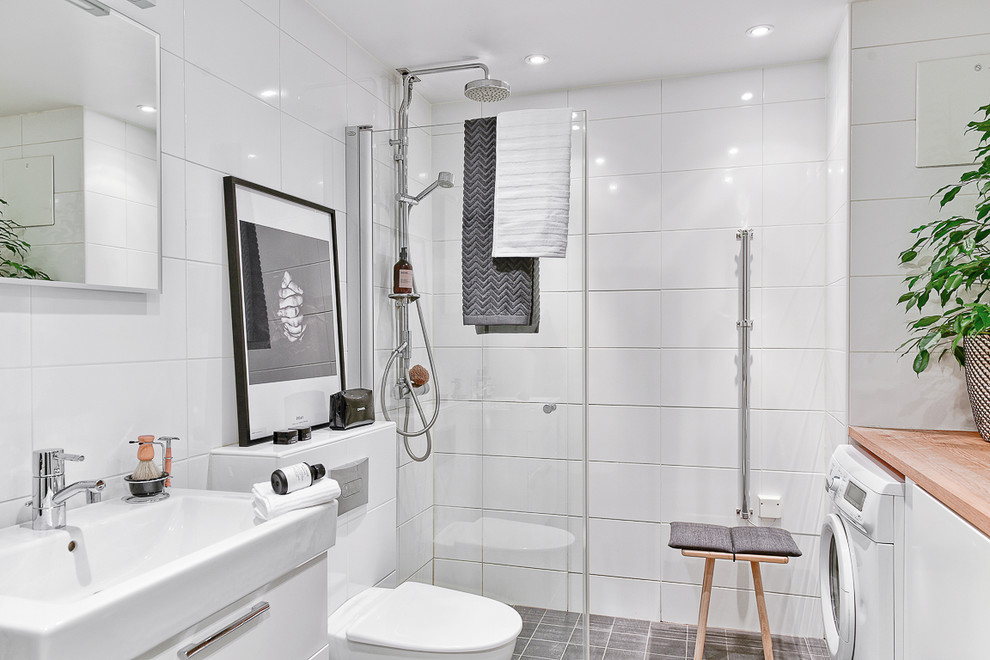 Inredning av ett nordiskt badrum med dusch, med släta luckor, vita skåp, en öppen dusch, vit kakel, ett konsol handfat, grått golv och med dusch som är öppen