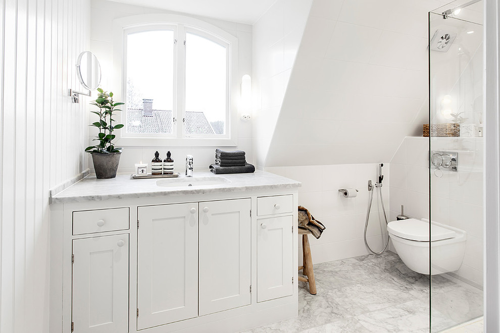 Inspiration för mellanstora minimalistiska badrum med dusch, med luckor med infälld panel, vita skåp, en dusch i en alkov, en vägghängd toalettstol, vit kakel, vita väggar, mosaikgolv, ett nedsänkt handfat, marmorbänkskiva, vitt golv och dusch med gångjärnsdörr