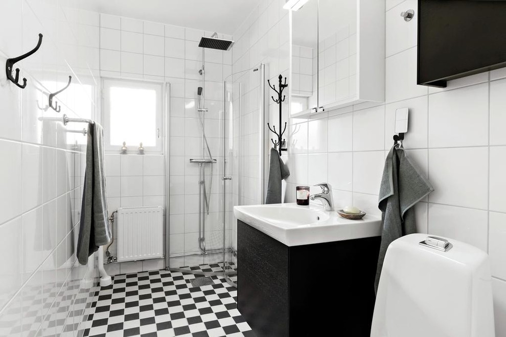 Inredning av ett skandinaviskt badrum med dusch, med släta luckor, svarta skåp, en hörndusch, vit kakel, vita väggar, ett konsol handfat, dusch med gångjärnsdörr och flerfärgat golv