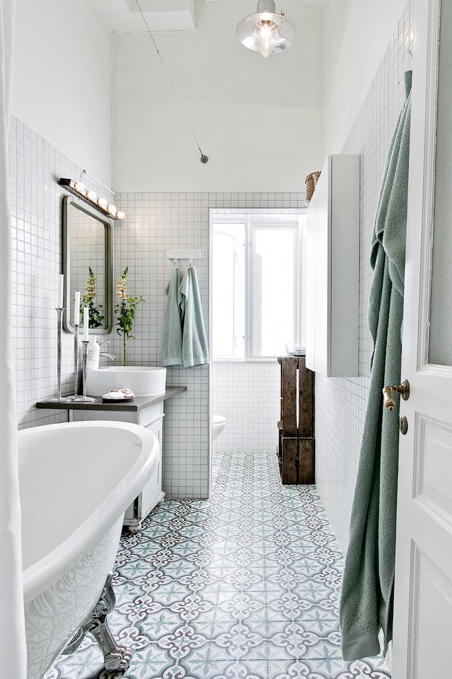 Nordisk inredning av ett mellanstort grå grått badrum med dusch, med ett badkar med tassar, en dusch/badkar-kombination, vit kakel, dusch med duschdraperi, släta luckor, vita skåp, vita väggar, ett konsol handfat och flerfärgat golv