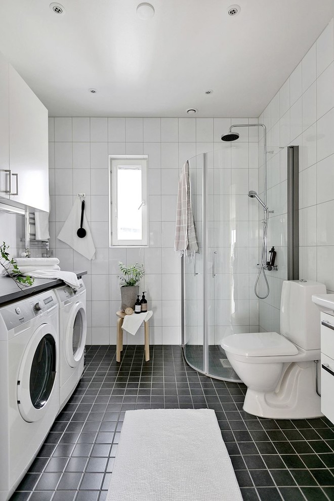 Inspiration for a scandinavian shower room bathroom in Stockholm with a corner shower, a two-piece toilet, white tiles, black floors and a laundry area.