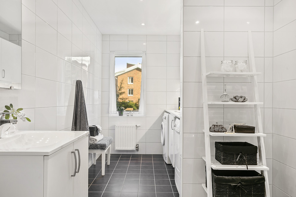 Cette photo montre une salle de bain scandinave avec un placard à porte plane, des portes de placard blanches, un carrelage blanc, un sol noir et buanderie.