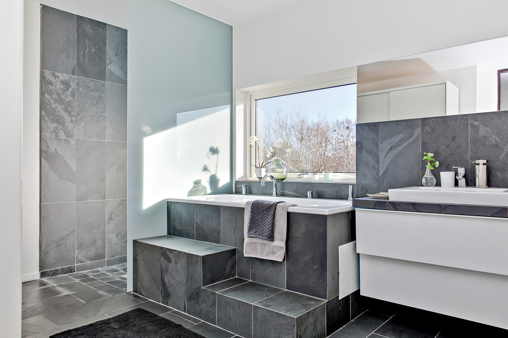 Inredning av ett modernt badrum, med släta luckor, vita skåp, ett platsbyggt badkar, våtrum, grå kakel, grå väggar och med dusch som är öppen