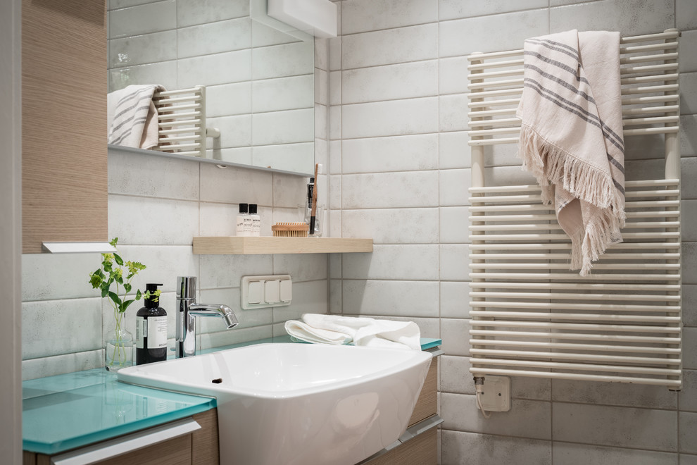 Imagen de cuarto de baño nórdico con armarios con paneles lisos, puertas de armario de madera clara, baldosas y/o azulejos blancos, lavabo encastrado, encimera de vidrio y encimeras blancas
